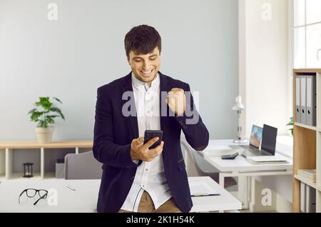 Happy successful business man looking at notification on mobile phone and smiling Stock Photo