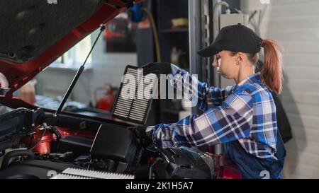 Caucasian female auto mechanic changes the engine air filter in the car. Stock Photo