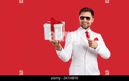 Happy handsome man in suit and glasses smiling and pointing at gift box in his hand Stock Photo