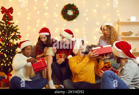 Group of cheerful friends exchange gifts and have fun during Christmas party at home. Stock Photo
