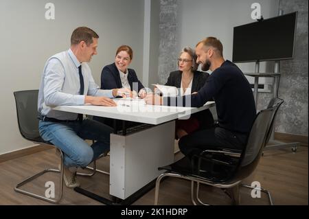 Four colleagues are discussing blueprints in a conference room in an office. Brainstorming of engineers and architects. Stock Photo