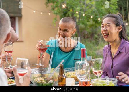Multiracial friends eating and drinking happy smiling and laughing in the patio. Middle-aged cheerful people around the table. Stock Photo