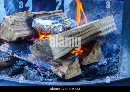 Baked potatoes cooking over a outdoor Wood campfire wrapped in foil. Stock Photo