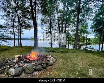 Campfire next to a calm lake in the summer, horizontal Stock Photo