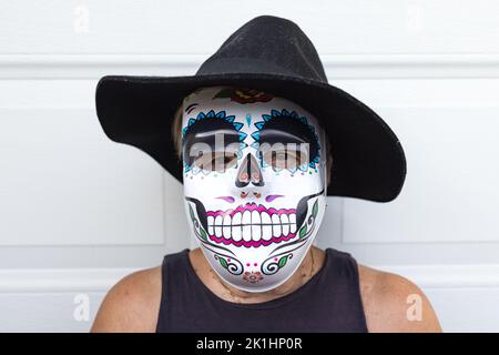 Portrait of an elderly lady with a catrina mask and hat, celebrating Halloween and All Souls' Day, on a white background. Celebration, costume, party Stock Photo