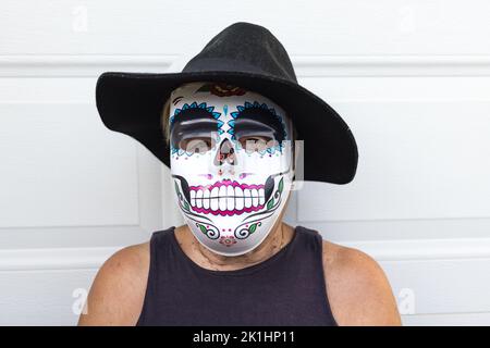 Portrait of an elderly lady with a catrina mask and hat, celebrating Halloween and All Souls' Day, on a white background. Celebration, costume, party Stock Photo
