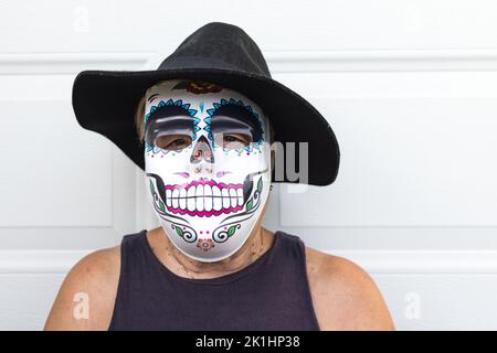 Portrait of an elderly lady with a catrina mask and hat, celebrating Halloween and All Souls' Day, on a white background. Celebration, costume, party Stock Photo