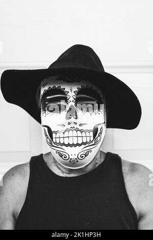 Black and white portrait of an elderly lady with a catrina mask and hat, celebrating Halloween and All Souls' Day, on a white background. Celebration, Stock Photo