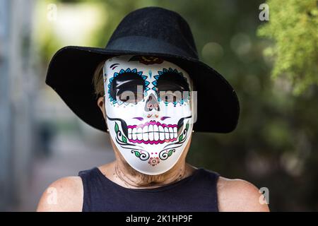 Portrait of an elderly lady with a catrina mask and hat, celebrating Halloween and All Souls' Day, on the street. Celebration, costume, party and mask Stock Photo