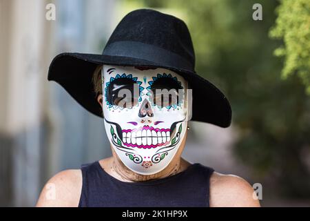 Portrait of an elderly lady with a catrina mask and hat, celebrating Halloween and All Souls' Day, on the street. Celebration, costume, party and mask Stock Photo