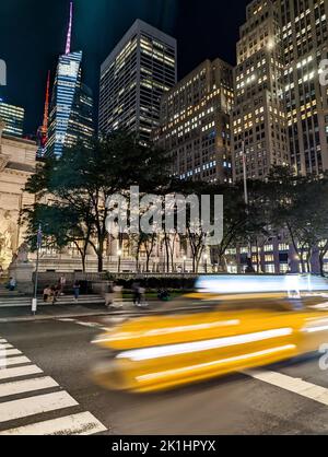 Blurred yellow taxi driving down the street in New York City at night with the lights of the buildings in the background Stock Photo