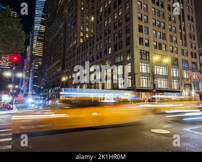 Blurred motion of a yellow taxis driving down the street through New York City at night with the building lights in the background Stock Photo