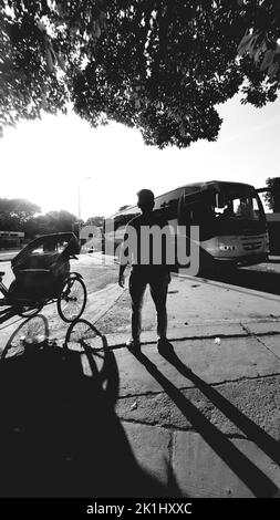 A silhouette of a man with its shadow on the street, grayscale shot Stock Photo