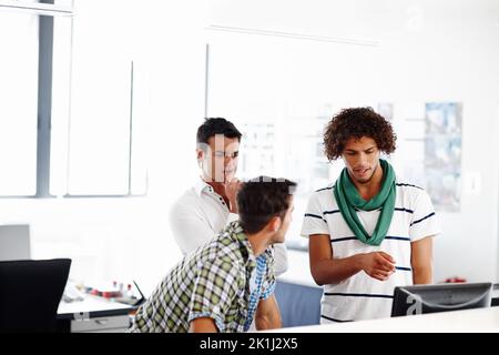 Brainstorming some ideas for the company website. Three male colleagues working in the office together. Stock Photo