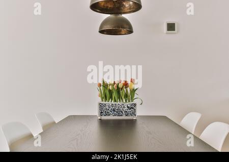 Wooden table with vase of flowers under black pendant lamp in modern living room Stock Photo
