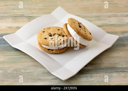 Two chocolate chip cookie vanilla ice cream sandwiches on white dessert plate Stock Photo