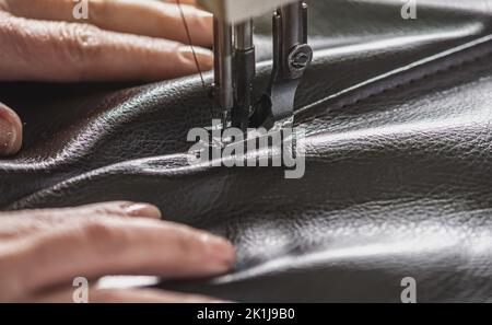 Women's hands in the process of sewing on professional equipment. Sewing leather in production. Close-up. Stock Photo