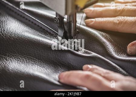 Women's hands in the process of sewing on professional equipment. Sewing leather in production. Close-up. Stock Photo