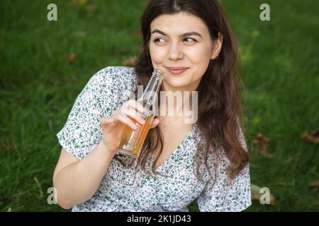 A young woman in nature drinks a drink from a glass bottle. Stock Photo