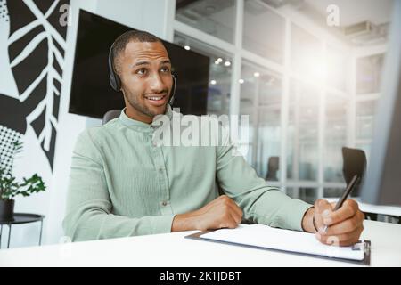 Confident African businessman taking notes while talking on phone with client in modern office Stock Photo