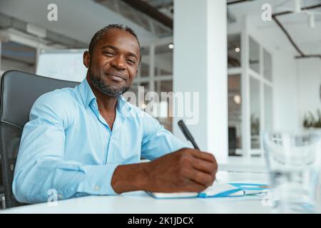 Confident African businessman taking notes while working in modern office Stock Photo