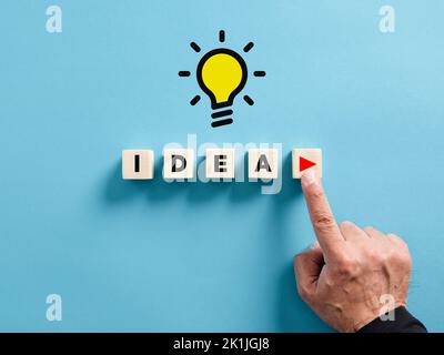 Male hand presses the play button with the word idea on wooden cubes. To execute an idea concept. Stock Photo