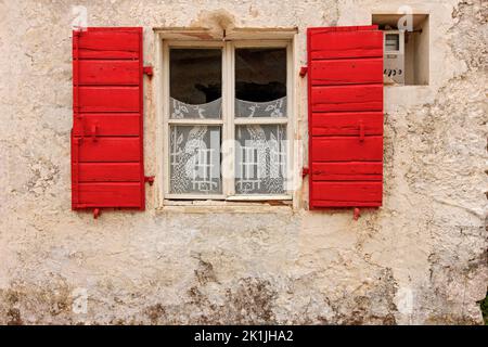 Picturesque facade of traditional local house with stone wall, red window and elaborate lace curtains, seen in a village of Zakynthos island, Greece Stock Photo