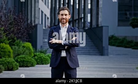 Stylish man in suit on street confident leader posing with crossed arms outdoors handsome successful male professional manager smiling looking at Stock Photo