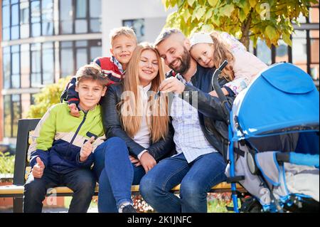 Happy family - father, mother and children having fun together on playground. Smiling father holding keys from new apartment in new city district. Modern residential buildings on background. Stock Photo