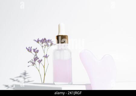 Pink Gua Sha facial massage tools. Rose Quartz jade scrapper and beauty facial oil on white background. Anti age, lifting and toning treatment at home Stock Photo