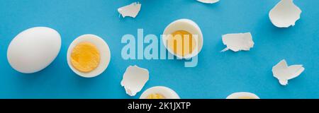 Top view of boiled eggs near while cracked shells on blue background, banner Stock Photo