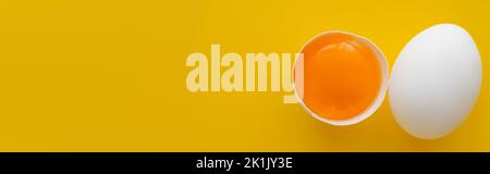 Top view of fresh yolk in shell and while egg on yellow background, banner Stock Photo