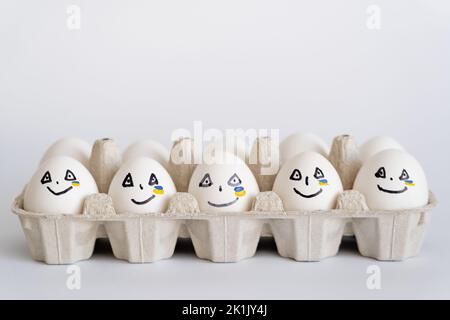 Painted eggs with facial expressions and ukrainian flag in tray on white background Stock Photo