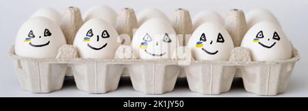 Painted eggs with facial expression and ukrainian flag in container on white background, banner Stock Photo