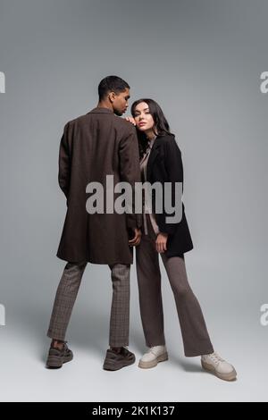 full length of stylish interracial couple in autumnal outfits posing together on grey,stock image Stock Photo