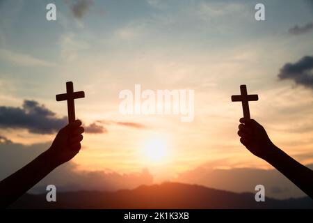 Silhouette off hands holding wooden cross  on sunrise background, Crucifix, Symbol of Faith. Stock Photo