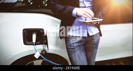 Businessman using digital tablet while charging electric car at charging station Stock Photo