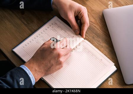 Close up top view of businessman writing in notebook, caucasian male hands holding pen making notes planning new appointments information in organizer Stock Photo