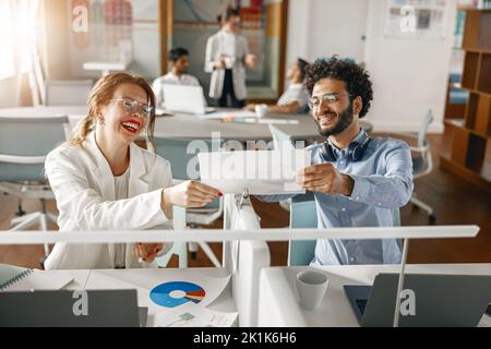 Two young diverse coworkers analyzing sales report while working together in the office Stock Photo