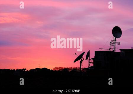 A satellite antenna on a house roof with a purple sunset sky in the background Stock Photo