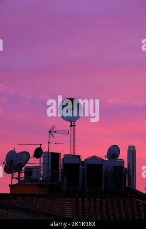 A vertical shot of a satellite antenna on a house roof with a purple sunset sky in the background Stock Photo
