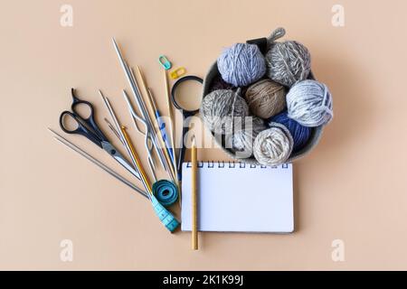 Knitting accessories, hook, needles, scissors, magnifying glass, centimeter, notebook with pencil, a basket with blue gray brown balls of thread on an Stock Photo