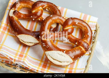 Two homemade freshly baked soft pretzels in bread basket with napkin. Traditional Bavarian pretzel for Octoberfest. Top view, close-up Stock Photo