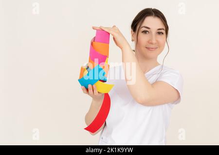 Portrait of young smiling pretty masseuse woman wearing white uniform, showing kinesio tapes rolls of different colours. Stock Photo