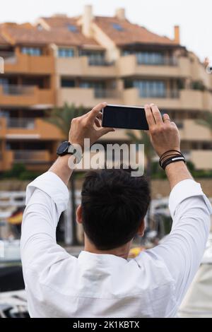 Rear view of an adult male taking a photo or selfie with a smartphone on vacation.  Stock Photo