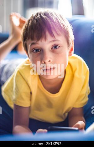 Boy lying on his front on a sofa holding a mobile phone Stock Photo