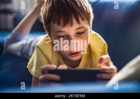 Boy lying on his front a sofa using a mobile phone Stock Photo