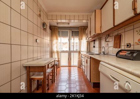 Antique kitchen with edge wood cabinets, folding table with stools, bay window in back, and light brown flooring Stock Photo