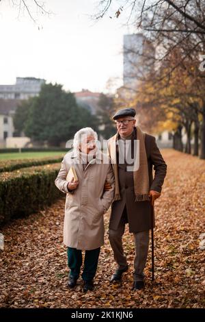 Happy senior couple on walk outdoors in town park in autumn. Stock Photo