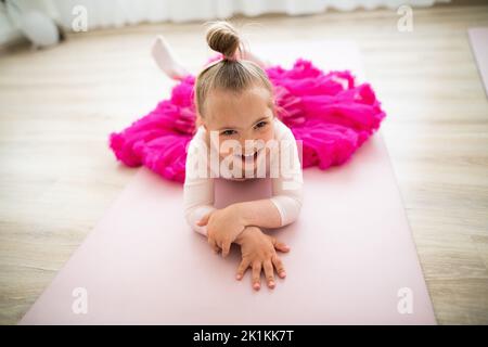 Little girl with down syndrome at ballet class in dance studio,lying and resting. Concept of integration and education of disabled children. Stock Photo